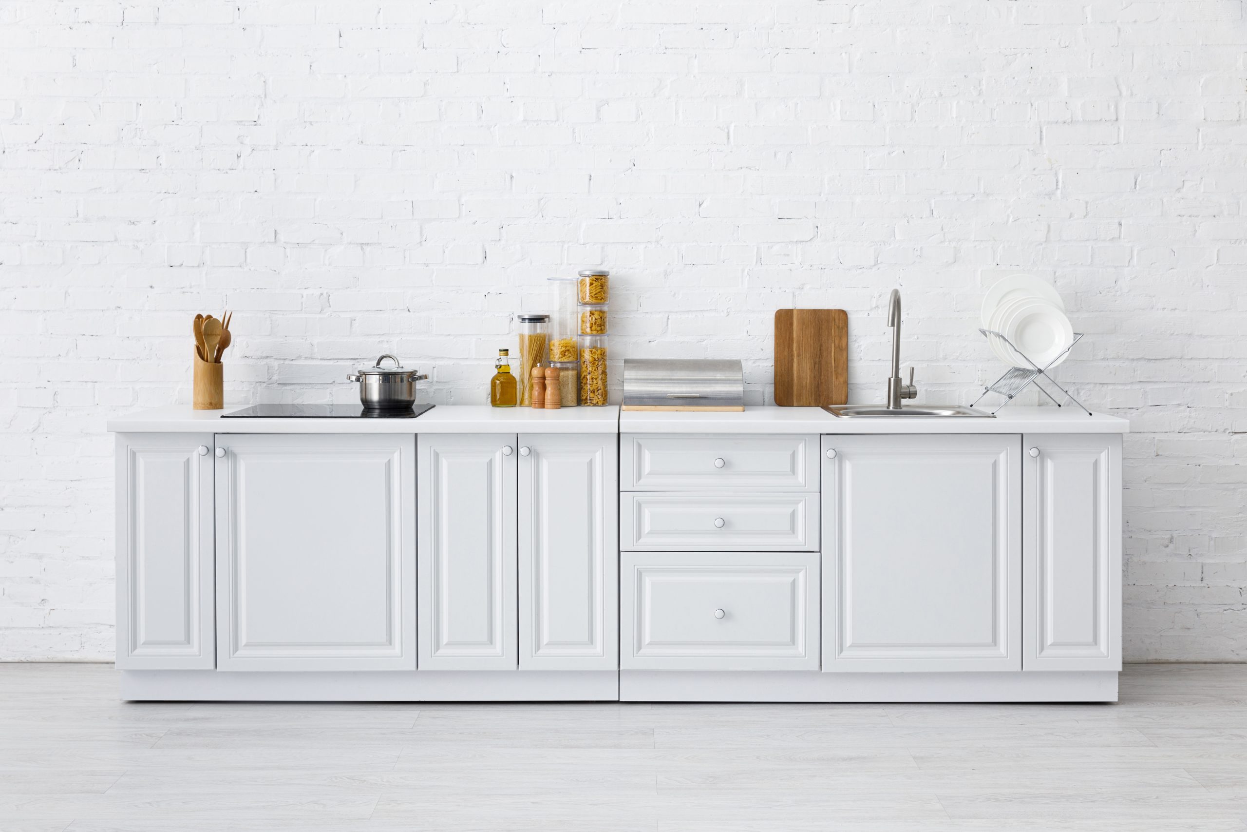 minimalistic modern white kitchen interior with kitchenware near brick wall